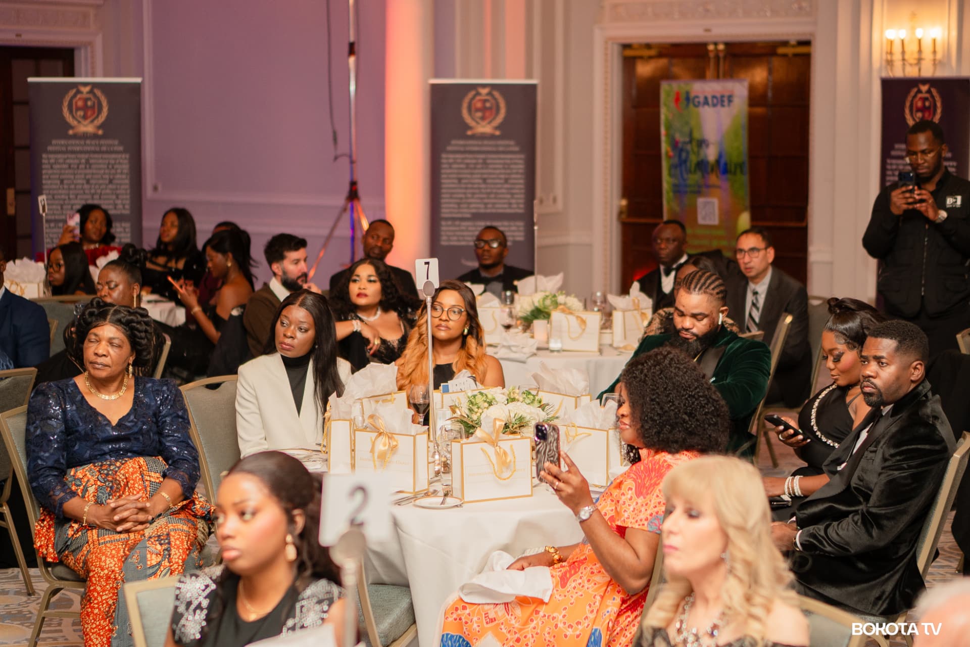 Guests in evening dress seated at tables with white and gold gift bags, with MBOMBO Gala Night banners behind them